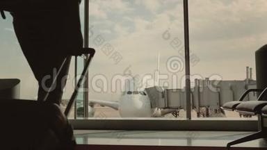 一个带着行李的女人去机场候机楼的一个大窗户。 窗外你可以看到一架漂亮的客机